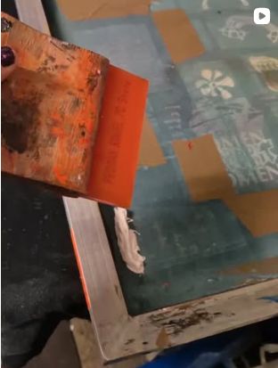 Rakel mit oranger Farbe auf einem Sieb